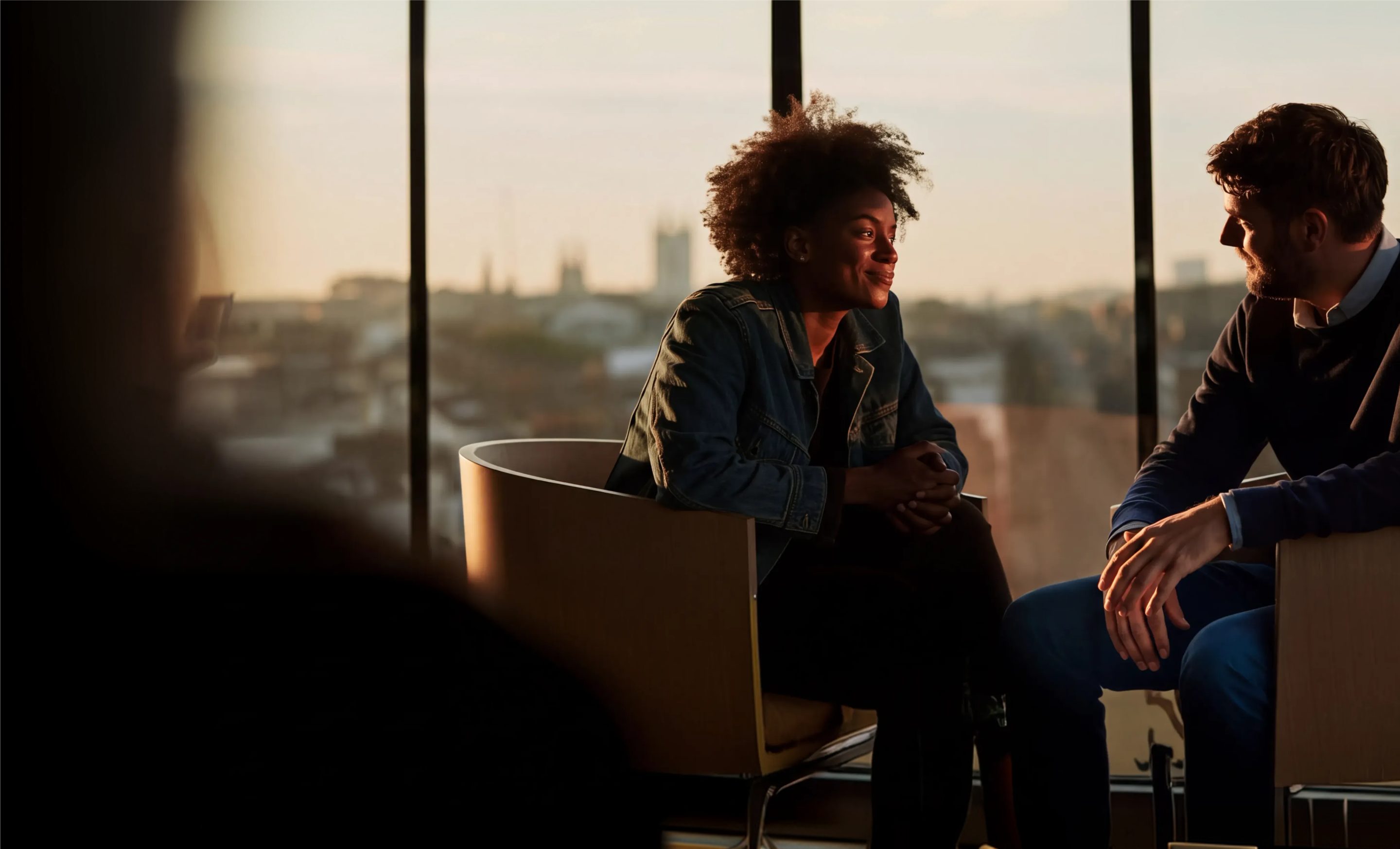 Two colleagues talking in armchairs by a window at sunset
